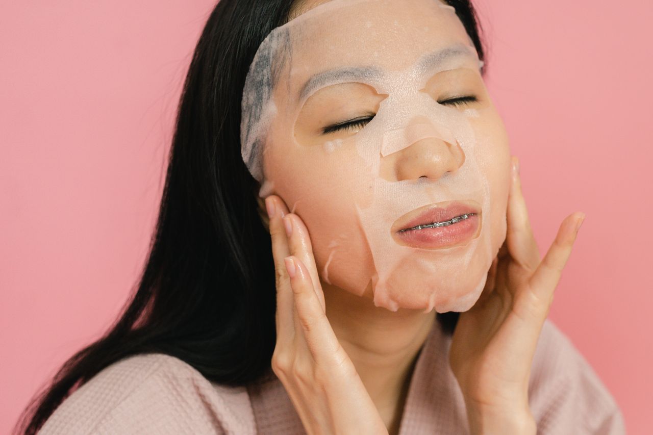 About Asian woman applying a hydrating facial sheet mask for skincare routine therapy.